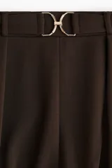 Pantalón sastre marrón de corte ancho, con pinzas y cinturón decorativo con hebilla metálica.