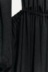 Vestido midi negro de cuello redondo y manga larga abullonada con puños. Tiene cintura elástica y detalle de espalda descubierta. El cierre es con botón en el cuello.
