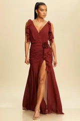 Vestido largo de fiesta color borgoña, con escote en V, mangas con volados, talle drapeado con flor decorativa y falda con abertura lateral.
