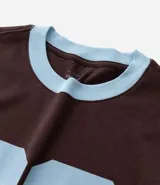 Remera de algodón color marrón con cuello redondo y ribetes en las mangas y cuello en color celeste. Presenta el número "86" estampado en grande en color celeste en el frente.