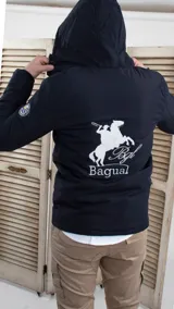Campera negra con capucha, cierre frontal y bolsillos laterales con cierre. Presenta un logo bordado en el pecho y un parche con diseño de paisaje en la manga.