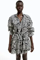 Vestido corto de algodón con estampado abstracto en blanco y negro. Tiene cuello con volados y lazo con borlas, mangas largas abullonadas con puños elásticos y falda escalonada con volados.
