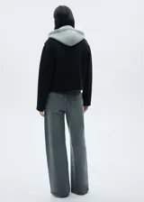 Chaqueta negra corta con capucha gris desmontable y ajustable con cordones. Presenta cuello camisero, cierre de cremallera doble, bolsillos laterales y bajo con goma elástica.