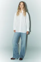 Camisa blanca de corte amplio, con cuello solapa, manga larga y cierre frontal con botones.