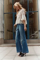 Jeans de tiro alto en denim de algodón rígido, color azul medio con efecto degradado (ombré) que se oscurece hacia el bajo. Corte acampanado (flare) y bajo deshilachado. Presenta bolsillos parche con botón en la parte delantera y trabillas ajustables con botón a los lados de la cintura.