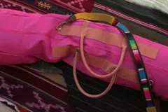 Bolso de mano fucsia con detalles en cuero color beige y correa de hombro multicolor.