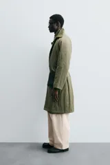 Trench color verde oliva de tejido técnico, corte relaxed fit, cuello solapa, manga larga, bolsillos laterales y abertura en la espalda.