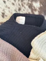 Poncho tejido en lana merino color crudo, con cuello alto y etiqueta de cuero con logo en la espalda.