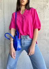 Blusa fucsia con cuello tipo vesper y mangas abullonadas, detalles de bordado y lazo.