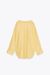 Camisa oversize a rayas amarillas y blancas, de cuello solapa y manga larga tipo murciélago acabada en puño con hombro caído. Tiene un bolsillo de plastrón en el delantero y cierre frontal con botones.