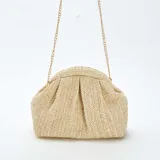 Bolso bandolera color beige, tejido en rafia con patrón de espiga. Tiene forma rectangular con cierre superior fruncido y cadena dorada para colgar al hombro.