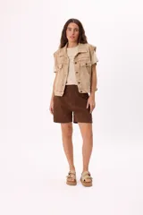 Chaleco de denim color beige con lavado desgastado, corte relajado y bolsillos frontales.