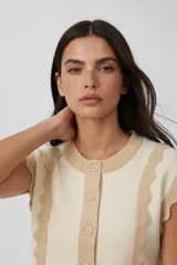 Chaleco sin mangas de acrílico, color beige y crema, con volados en los laterales y cierre frontal con botones.