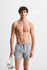 Short de baño con textura seersucker a rayas verticales azul marino y blanco. Tiene cintura elástica ajustable con cordón, bolsillos frontales y traseros, aberturas laterales en el bajo y forro interior.