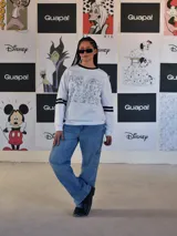 Buzo blanco de manga larga con cuello redondo y puños y ruedo en rib negro. Presenta un gran estampado frontal de la letra 'M' rellena de dibujos de personajes de Disney, incluyendo a Mickey Mouse. Las mangas tienen dos franjas negras a la altura del bíceps.
