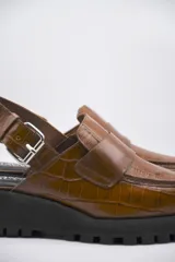 Zueco tipo mocasín color marrón con textura croco y tira regulable al talón.