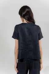 Blusa de lino color beige con rayas verticales negras, corte recto, escote redondo y mangas cortas.
