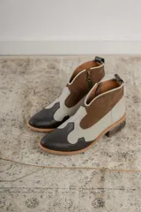 Botines de cuero marrón y blanco con diseño western, puntera redondeada y cierre lateral con cremallera. El talón tiene una tira de cuero para facilitar el calce.