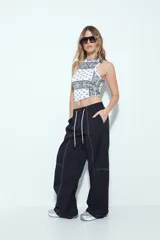 Pantalón tipo babucha negro de tiro bajo con costuras visibles en contraste blanco. Presenta cintura elástica con lazo ajustable blanco y silueta amplia con caída relajada.