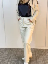 Pantalón de cuero sintético color beige, de corte recto, con bolsillos laterales y botón frontal.