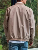 Campera bomber color beige, de Jack & Jones, con cuello de béisbol y cierre frontal con cremallera. Tiene bolsillos laterales con cremallera y un bolsillo en la manga.