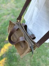 Cartera bandolera de cuero color verde oliva, con forro de tela, bolsillo delantero con cierre y bolsillo interno. Tiene correa larga regulable y manijas cortas.