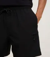 Bermuda de hombre color beige confeccionada en tejido ripstop, con cintura elástica ajustable con cordón, bolsillos laterales y etiqueta de la marca aplicada.