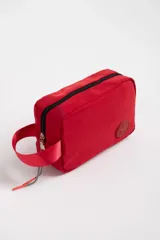 Necesser rojo rectangular de tela impermeable, con cierre superior negro, asa de mano y logo circular en relieve.