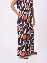 Pantalón de pierna ancha con estampado geométrico en tonos púrpura, naranja y blanco. Presenta cintura elástica y bolsillos laterales tipo cargo.