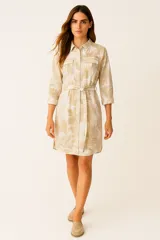 Vestido camisero corto con estampado de hojas color beige, cuello camisero, mangas 3/4, bolsillos en el pecho, cierre frontal con botones y cinturón de lazo.