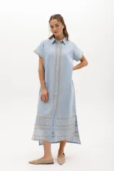 Vestido largo de lino en color celeste, con cuello camisero, manga corta y cierre frontal con botones. Presenta bordados decorativos en contraste en la pechera y en el ruedo.