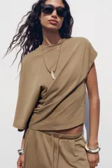 Camiseta color marrón con cuello redondo, manga sisa caída en un lado y manga corta en el otro. Tiene detalle de frunces laterales.