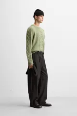 Sweater verde claro de punto con cuello redondo y mangas largas. Presenta diseño de trenzas en el centro y en las mangas.