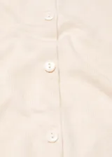 Cárdigan de punto fino color crema, con cuello redondo, manga larga y cierre frontal con botones.