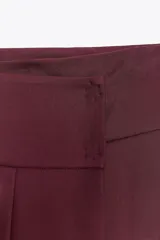 Falda midi color borgoña de tiro alto con tablas en el delantero y cierre frontal cruzado con botones a presión.