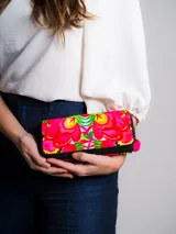 Billetera rectangular de tela color crema con bordado floral multicolor. Cierre superior con cremallera y tirador con pompón rojo y cuentas de madera.