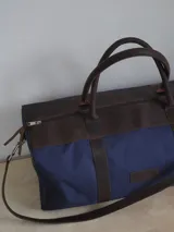 Bolso de lona color negro con detalles en cuero color tostado. Tiene doble asa de mano y correa de hombro ajustable y extraíble.