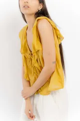 Blusa amarilla sin mangas con volados y lazo en el escote.