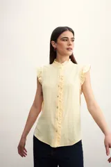 Camisa color amarillo pálido con cuello mao, sin mangas, con volados en los hombros y en el frente.