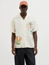 Camisa de manga corta color crema con estampado de flores y hojas en tonos naranja y verde. Tiene cuello resort, cierre frontal con botones y calce relajado.