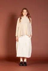 Buzo de tejido color beige claro, con cuello tortuga alto y mangas largas ajustadas. El cuerpo del buzo es de silueta amplia con bajo asimétrico.