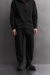 Pantalón jogger color marrón oscuro, corte regular fit, confeccionado en tejido técnico compacto de algodón con elasticidad. Cuenta con cintura elástica ajustable con cordón, bolsillos frontales y bolsillo lateral con cierre de cremallera.