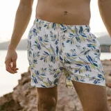 Short de baño blanco con estampado de hojas en tonos azul y verde. Tiene elástico en la cintura, cordón ajustable, tres bolsillos y mesh interior hipoalergénico.