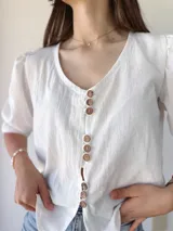 Camisa blanca de mangas 3/4 con detalle de volados en los puños y botones de madera.
