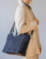 Cartera negra de gamuza con forro interior y correa larga desmontable.