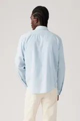 Camisa celeste claro de manga larga, confeccionada en lino, con cuello clásico, cierre frontal con botones y bolsillo de parche en el pecho izquierdo con logo de la marca.
