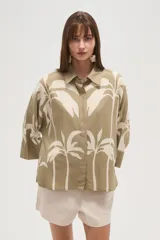 Camisa blanca con estampado de palmeras en color azul marino, de corte holgado, con cuello camisero, cierre frontal con botones y mangas 3/4 con puños anchos.