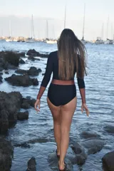 Traje de baño enterizo negro con mangas largas color cobre y cinturón ancho color cobre.