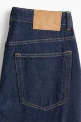 Pantalón jean de tiro alto, color azul oscuro, con corte holgado y pierna recta. Tiene cinco bolsillos y cierre con botón.