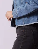 Campera de jean celeste de la marca Baccini, con cierre central, bolsillos delanteros, apliques colgantes de tachas en los hombros y terminación desflecada en el ruedo.